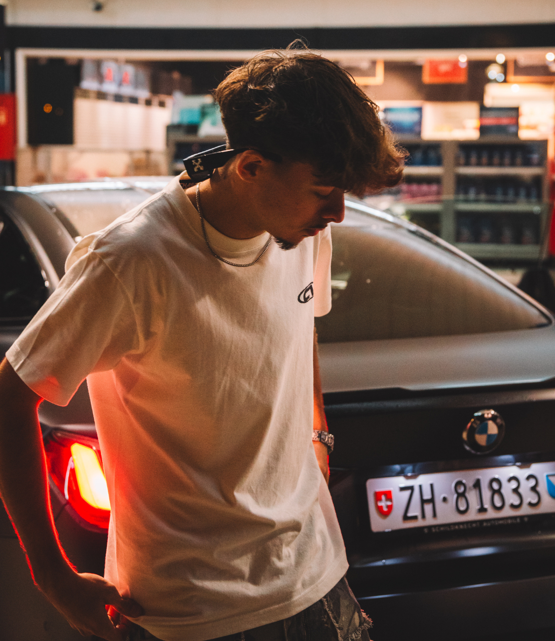 Young man wearing a white cotton T-shirt beside a BMW car at night, showcasing a casual street style.
