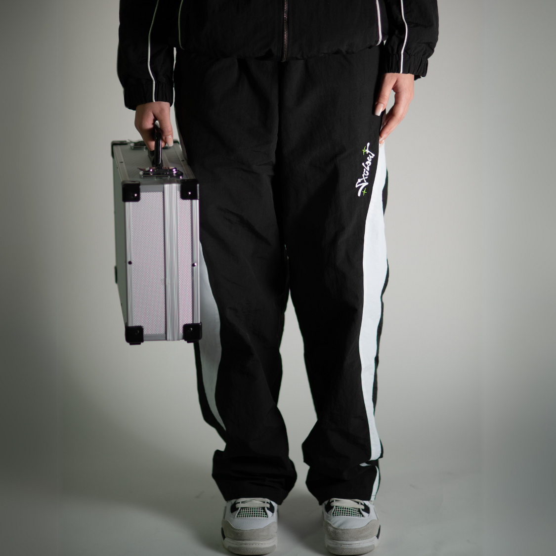 Person wearing Chasedvision VISION Baggy Nylon Trackpants in black, holding a silver case. Perfect for streetwear.