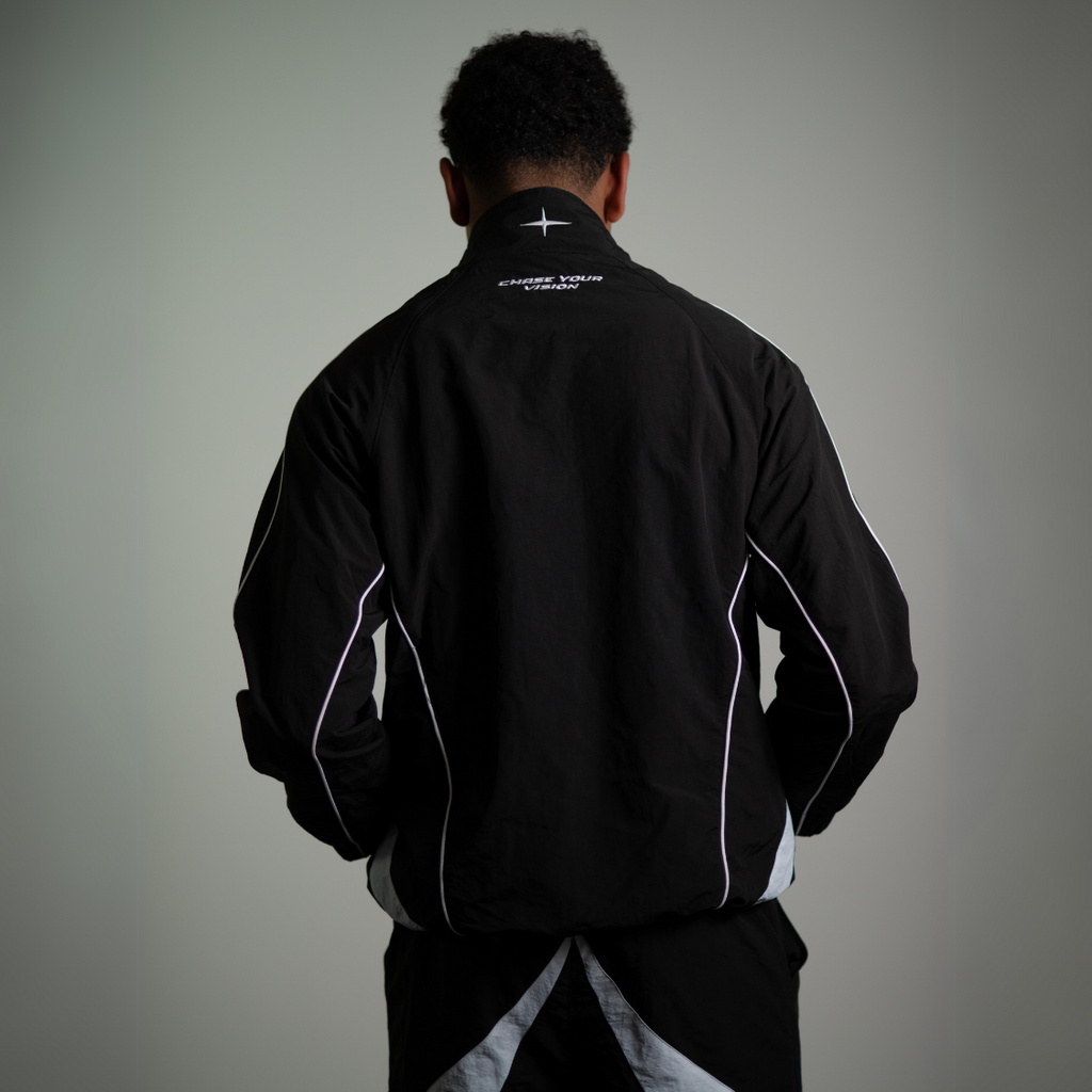 Back view of a man wearing black VISION TRACKJACKET, nylon streetwear, designed by Chasedvision, showcasing reflective accents.