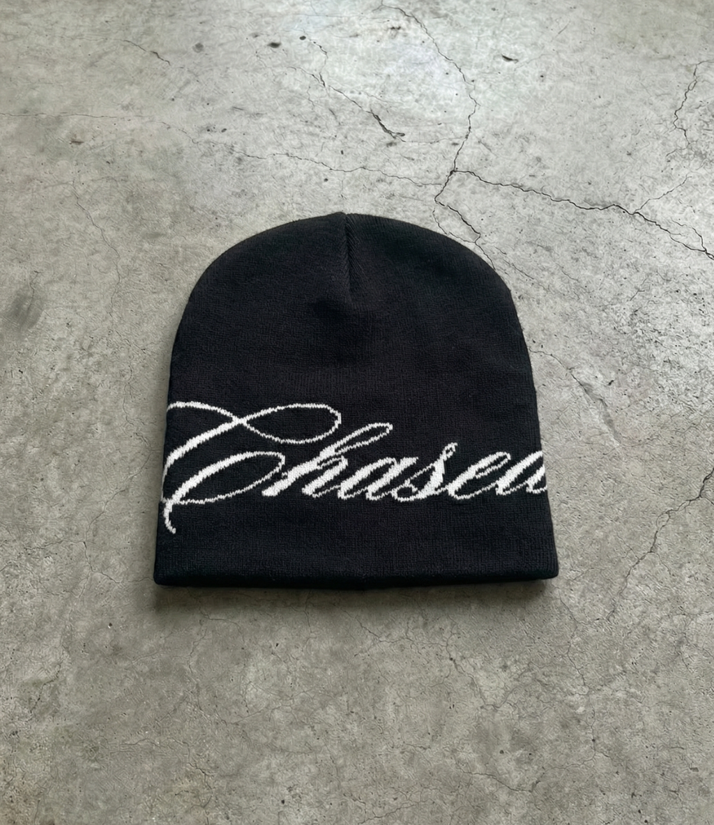 a black skully beanie with a chasedvision design laying on the floor, perfect for cold weather or to complete an outfit.