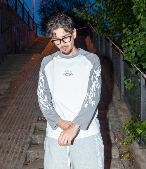 Model wearing a grey longsleeve shirt and shorts on a staircase, showcasing a stylish summer look.