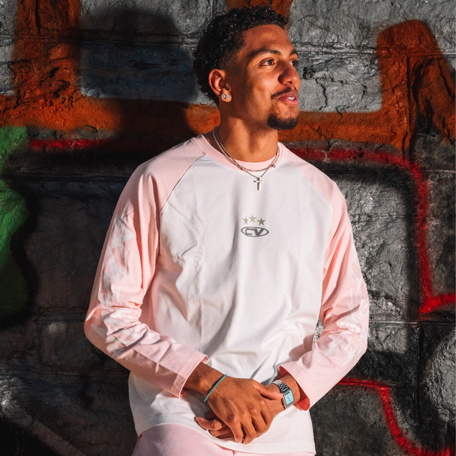 Stylish young man wearing a pink longsleeve shirt against a graffiti backdrop, perfect for summer outfits with shorts.